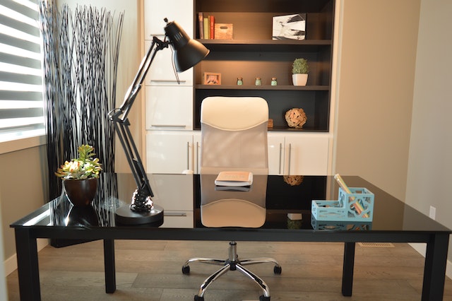 A home office with a beige chair and a big black table