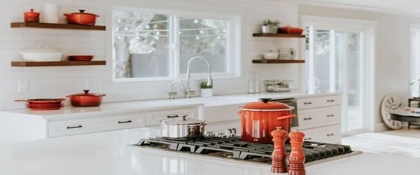 Kitchen with large windows, open shelves with red dishes on them, and a large kitchen island with a stove